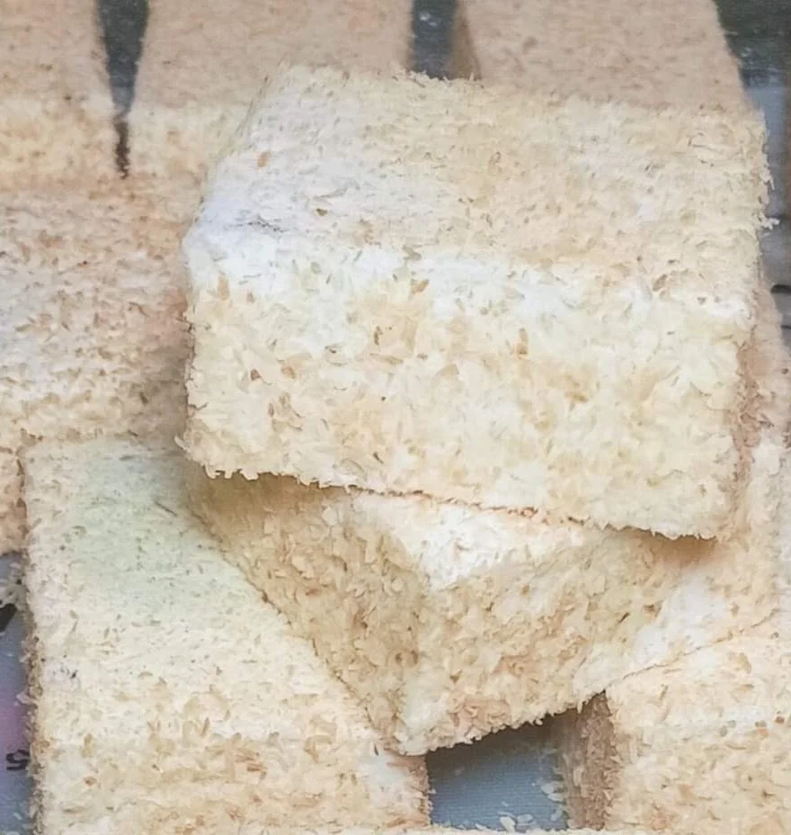 Marshmallow squares generously coated in coconut flakes on a wire rack